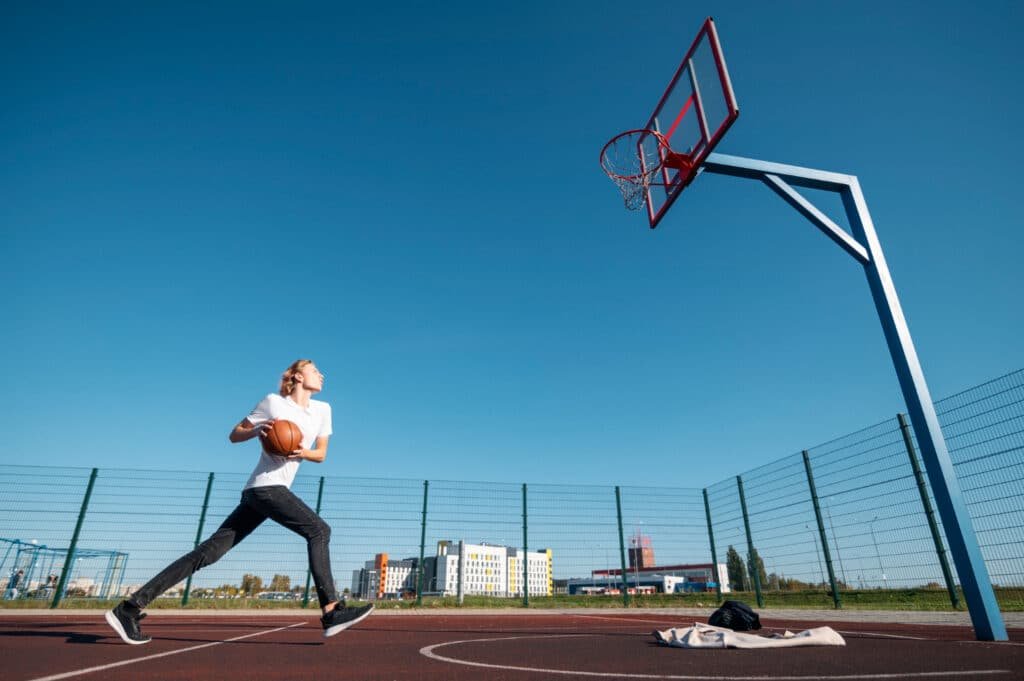 Un jeune homme jouant au basket sur un terrain extérieur.